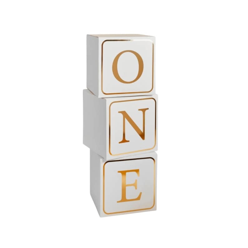 May include: White cardboard boxes stacked to spell out the word "ONE" in gold letters. Each box has a gold border.