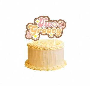 May include: A two-tiered cake with a brown and pink cake topper that says "Two Groovy" with a peace sign and flowers.