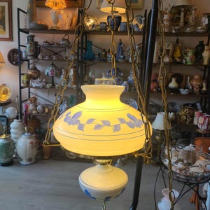May include: A white glass hanging lampshade with a blue floral design. The lampshade is suspended from a gold chain and has a white glass globe at the bottom.