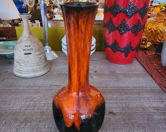 Puede incluir: Un jarrón de cerámica con un esmalte negro y naranja. El jarrón tiene un cuerpo redondo y un cuello largo y delgado.