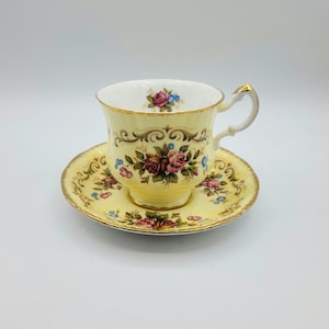 Op de afbeelding: Een vintage kop en schotel set. De kop en schotel zijn geel met bloemmotieven in roze, bruin en blauw. De kop heeft een gouden oor en rand. De schotel heeft een bijpassend bloemmotief en gouden rand. Een klassieke theeset.