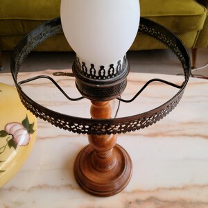 May include: A vintage wooden lamp base with a white glass shade and a black metal ring. The lamp has a decorative design on the base and the ring.