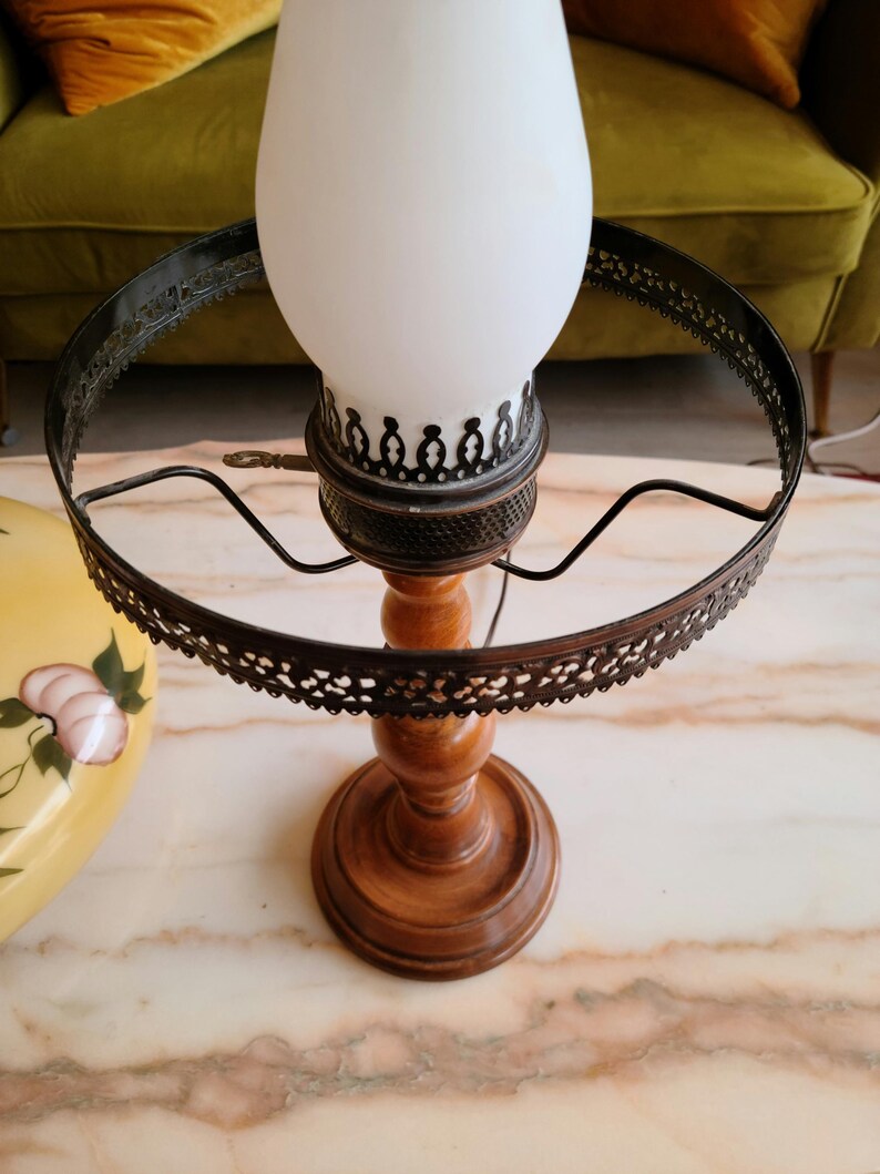 May include: A vintage wooden lamp base with a white glass shade and a black metal ring. The lamp has a decorative design on the base and the ring.