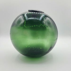 Puede incluir: Una boya de vidrio redonda y verde de gran tamaño con una pequeña parte superior negra.