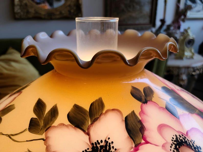 May include: A yellow glass lampshade with a ruffled edge and a floral design. The flowers are painted in shades of pink, white, and green.