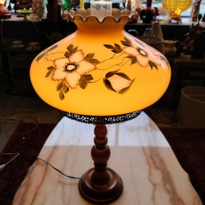 May include: A vintage table lamp with a yellow glass shade featuring a floral design. The shade has a scalloped edge and a metal trim. The lamp has a wooden base.