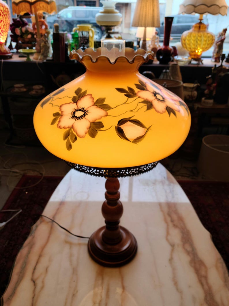 May include: A vintage table lamp with a yellow glass shade featuring a floral design. The shade has a scalloped edge and a metal trim. The lamp has a wooden base.