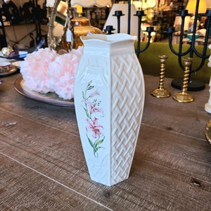 Puede incluir: Jarrón de cerámica blanca con un patrón tejido y un diseño floral rosa. El jarrón tiene un borde festoneado y mide aproximadamente 25 cm de alto.