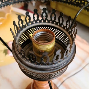 May include: Close-up of a black metal lamp base with a decorative design. The base has a round, open top with a brass light socket.