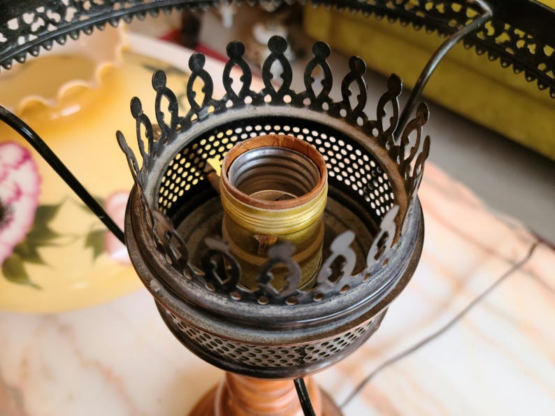 May include: Close-up of a black metal lamp base with a decorative design. The base has a round, open top with a brass light socket.