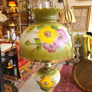 May include: A vintage hanging lamp with a green glass shade and a brass chain. The shade features yellow and pink floral designs. The lamp has a scalloped edge and a smaller, matching bottom globe.