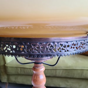 May include: A vintage table lamp with a round, scalloped, amber glass shade. The shade has a decorative metal trim with an intricate floral design. The lamp has a wooden base with a turned pedestal.