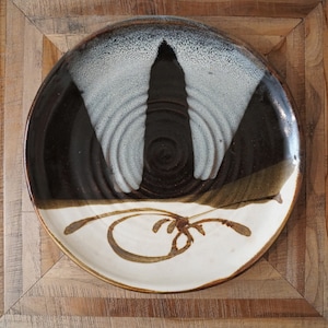 May include: A white ceramic plate with a brown and black design. The design features a stylized tree with a white background and brown branches. The plate has a slightly raised rim.