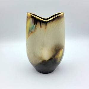Könnte beinhalten: Eine kleine, keramische Vase mit einem einzigartigen, abstrakten Design. Die Vase ist hellbeige mit braunen und goldenen Akzenten. Die Oberseite der Vase ist V-förmig.