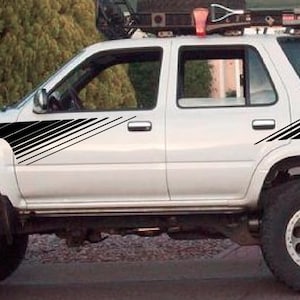 Puede incluir: SUV blanco con rayas diagonales negras en los lados. El vehículo tiene un portaequipajes en el techo con una cruz negra en la ventana trasera.