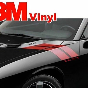 Puede incluir: Coche negro con rayas de carreras rojas y plateadas. El coche tiene un logotipo de 3M Vinyl en el parabrisas delantero. El texto "TEXT" está en el lateral del coche.