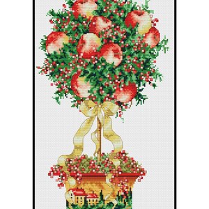Könnte beinhalten: Ein Kreuzstichmuster eines Topfapfelbaums mit roten Äpfeln, grünen Blättern und einem gelben Band. Der Topf hat eine bemalte Szene mit Häusern und Bäumen.