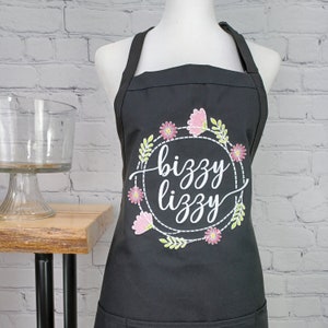 May include: Black apron with a white embroidered floral wreath and the text "bizzy lizzy" in a white cursive font.