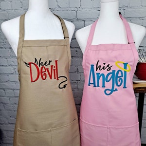 May include: Two brown and pink aprons with embroidered text. The brown apron has "Her Devil" in red and black embroidery. The pink apron has "His Angel" in blue and yellow embroidery.
