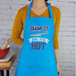 Pu&ograve; includere: Un grembiule da cucina blu con un'immagine di coltello bianco e il testo "Chop It Like It's Hot" in rosso e blu.
