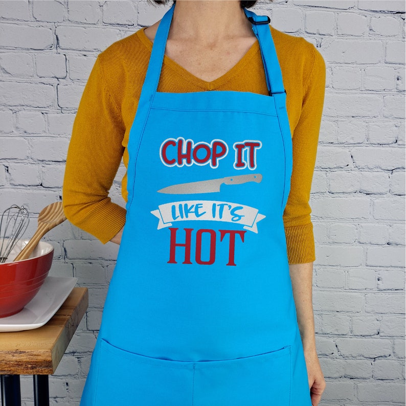 Pu&ograve; includere: Un grembiule da cucina blu con un'immagine di coltello bianco e il testo "Chop It Like It's Hot" in rosso e blu.