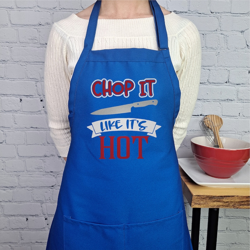 Pu&ograve; includere: Grembiule da cucina blu con un'immagine di coltello bianco e il testo "Chop It Like It's Hot" in rosso.