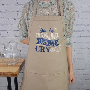 May include: A tan apron with blue text and a graphic of onions. The text reads "One day... I'm gonna make the onions cry."