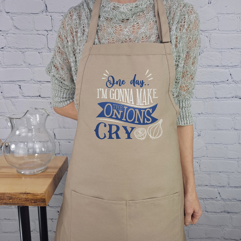 May include: A tan apron with blue text and a graphic of onions. The text reads "One day... I'm gonna make the onions cry."