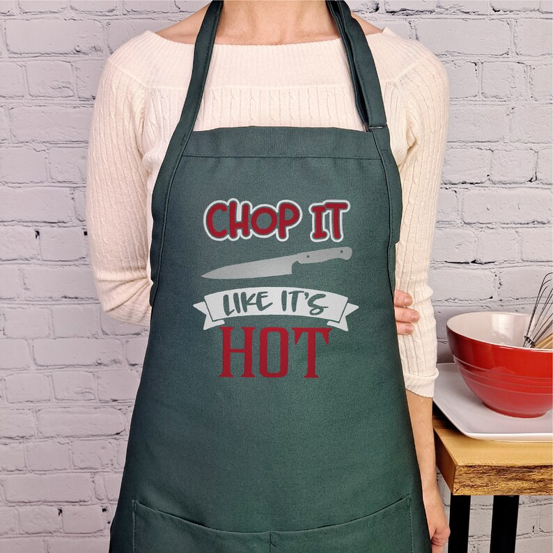 Pu&ograve; includere: Un grembiule da cucina verde scuro con il testo "Chop It Like It's Hot" in rosso e un'immagine di coltello grigia.