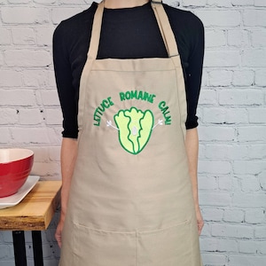 May include: A tan apron with a green embroidered lettuce with the text "Lettuce romaine calm!"