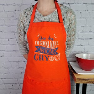May include: Orange kitchen apron with a blue and white design that says "One day... I'm gonna make the onions cry".