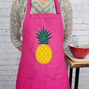 Può includere: Grembiule rosa acceso con un design di ananas giallo e foglie verdi. Il grembiule ha una tasca e spalline regolabili. Il design dell'ananas è al centro.