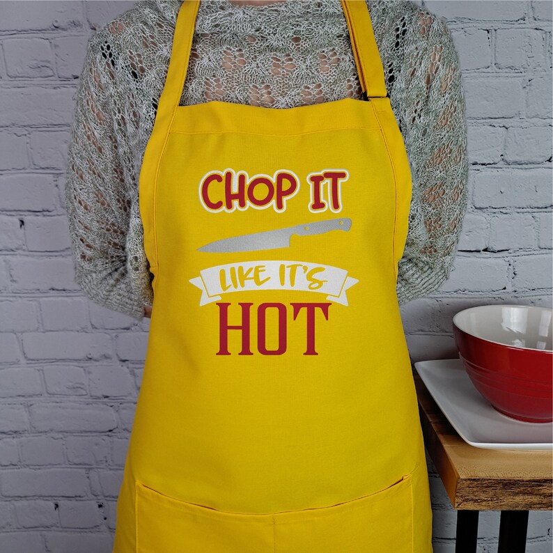 Pu&ograve; includere: Grembiule da cucina giallo con un'immagine di coltello bianco e il testo "Chop it like it's hot" in rosso.