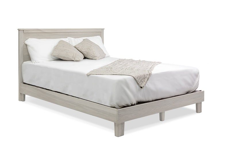 May include: A white wooden platform bed frame with a white mattress, two white pillows, and a beige throw blanket.