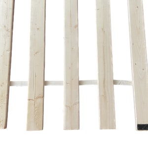 May include: A close-up of a wooden slat bed frame with six slats. The slats are made of natural wood and are held together by a white fabric strip.
