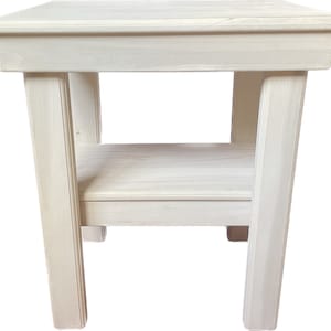 May include: White wooden end table with a shelf. The table has a simple design with straight lines and a smooth finish.
