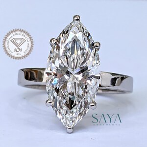 May include: A marquise-cut diamond ring with a white gold band. The diamond is the focal point, showcasing its facets and brilliance. The ring is set with four prongs. The logo of the International Gemological Institute is visible in the background.