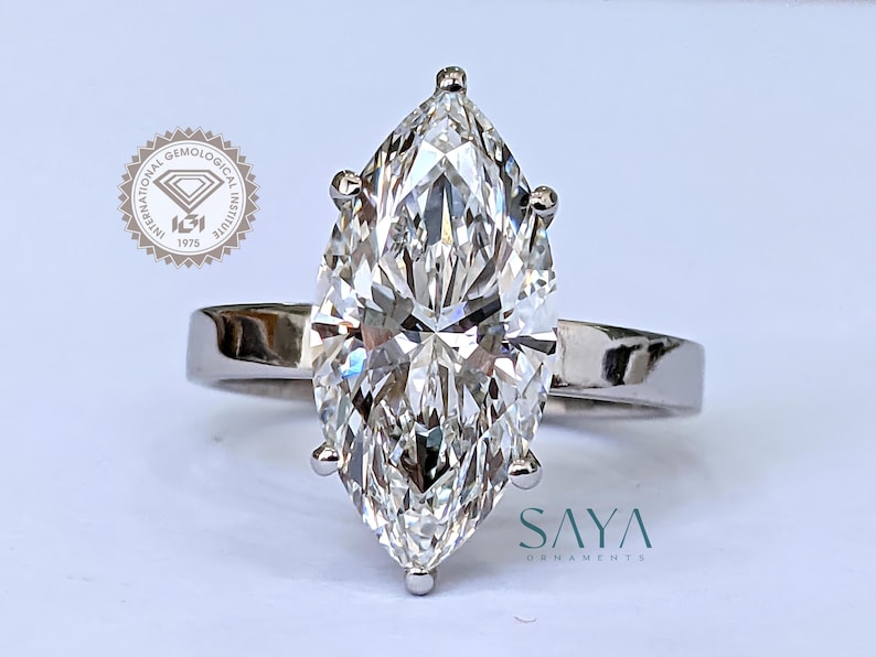 May include: A marquise-cut diamond ring with a white gold band. The diamond is the focal point, showcasing its facets and brilliance. The ring is set with four prongs. The logo of the International Gemological Institute is visible in the background.