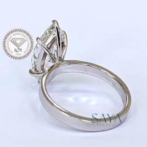 May include: A close-up of a platinum ring with a large, pear-shaped diamond. The ring is set with prongs and features a smooth, polished band. The image includes the text "SAYA ORNAMENT" and a logo from the International Gemological Institute.