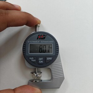 May include: A silver digital caliper with a black display reading 8.01 mm. The caliper is measuring a small, clear, round object. The caliper has a range of 0-12.7 mm / 0.5 inches and a resolution of 0.01 mm / 0.0005 inches.