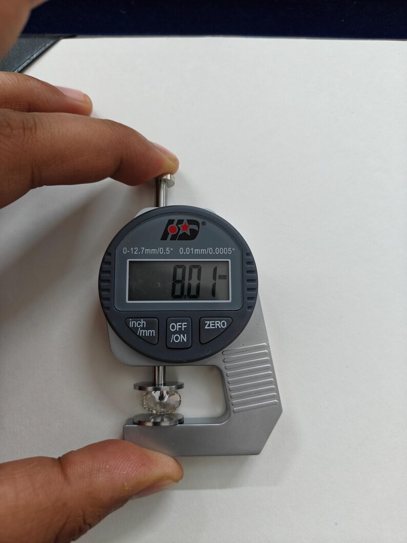 May include: A silver digital caliper with a black display reading 8.01 mm. The caliper is measuring a small, clear, round object. The caliper has a range of 0-12.7 mm / 0.5 inches and a resolution of 0.01 mm / 0.0005 inches.