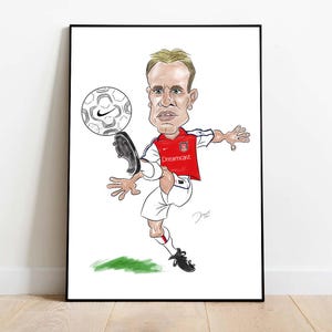 May include: A framed cartoon illustration of a soccer player kicking a soccer ball. The player is wearing a red and white jersey with the Dreamcast logo. The soccer ball has a Nike logo. The artwork is on a white background.