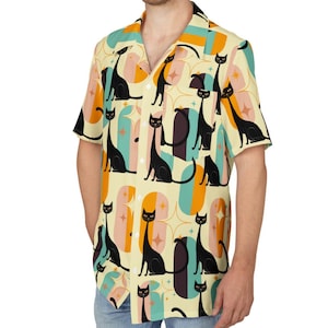 May include: Short-sleeved button-down shirt with a repeating pattern of black cat silhouettes on a cream background. The design includes orange, teal, and pink geometric shapes. The shirt has a classic collar and a relaxed fit.