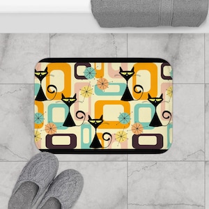 May include: A bath mat with a retro design featuring black cats and colorful geometric shapes. The background is a light cream color.