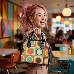 May include: A retro-style handbag with a geometric pattern of circles in orange, teal, brown, and cream. The bag has black handles and trim, and a structured shape. The bag is held by a person with pink hair.