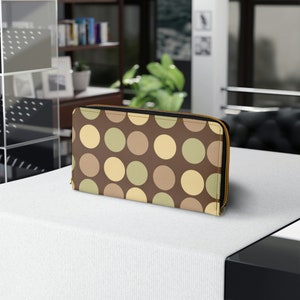 May include: A brown wallet with a gold zipper, featuring a pattern of large, colorful polka dots in shades of brown, beige, and green. The wallet is rectangular and appears to be made of leather or a similar material.
