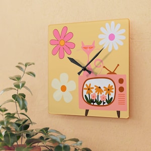 May include: Square wall clock with a yellow background featuring a pink cat, flowers, and a retro television. The clock hands are black. The clock is square and has a retro, vintage design.