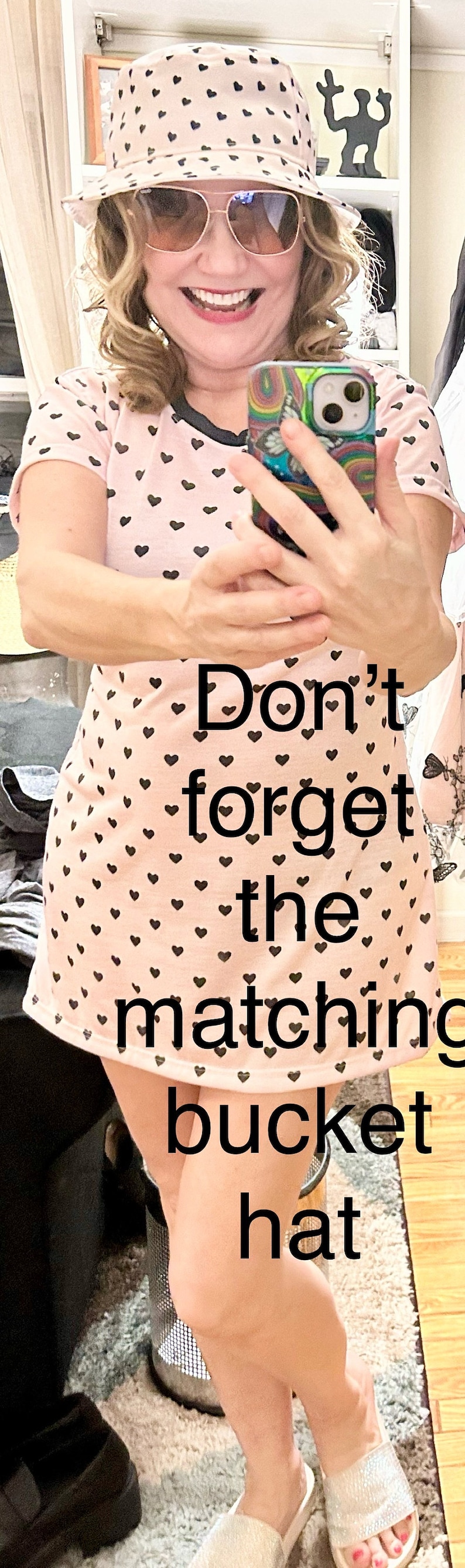 May include: A woman wearing a pink bucket hat with black hearts printed on it, a pink t-shirt with black hearts, and white sandals. The text "Don't forget the matching bucket hat" is superimposed on the image.