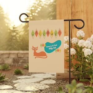 May include: A beige garden flag with a retro design featuring a stylized orange cat, the words "Welcome!" in a colorful diamond pattern, and the text "Come in & Chat Kitty Cat" in a blue speech bubble.
