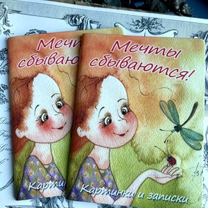 May include: Two small, colourful notebooks with a cartoon girl and a dragonfly on the cover. The text on the cover reads "Dreams come true!" and "Pictures and notes".